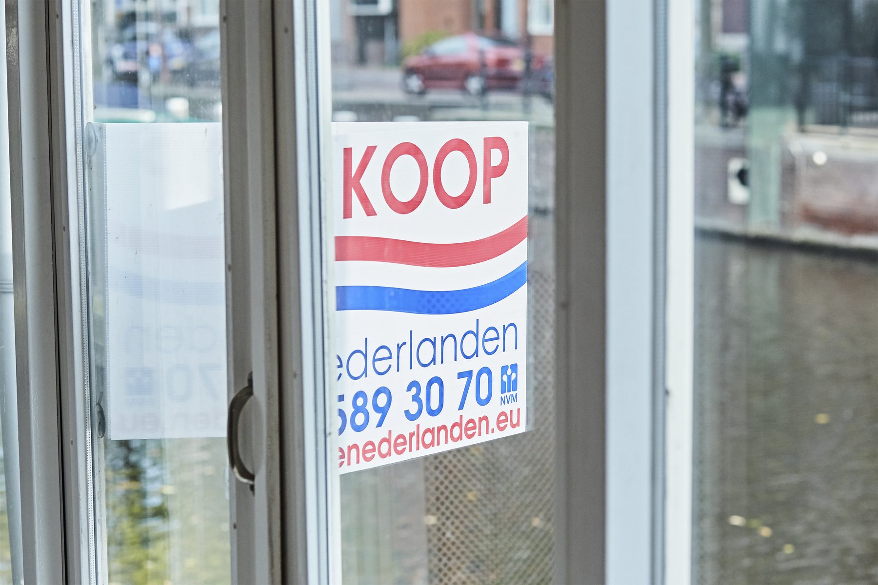 Het bord van De Nederlanden achter het raam van een pand aan de gracht